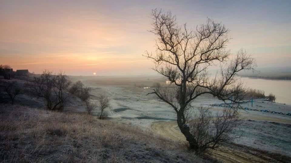 Havas táj napfelkeltével, fák és folyó látható a háttérben.