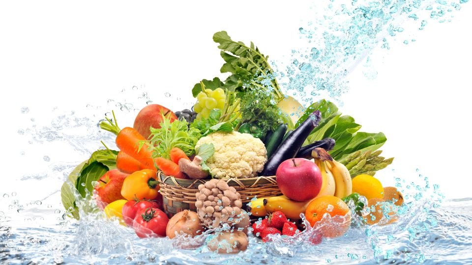 Friss zöldségek és gyümölcsök egy kosárban, vízsugarakkal körülvéve, színes és ízletes választék.