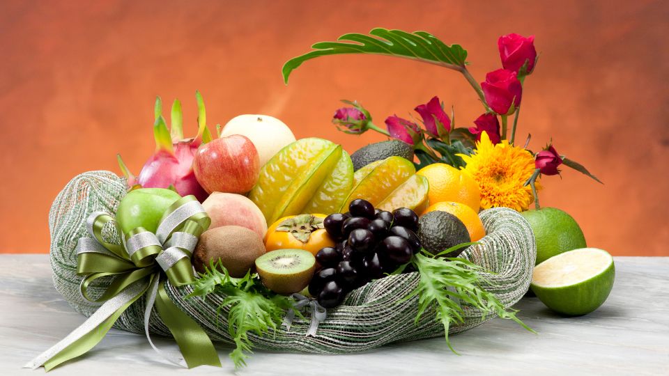 Friss gyümölcsök színes válogatása egy kosárban, virágokkal díszítve.