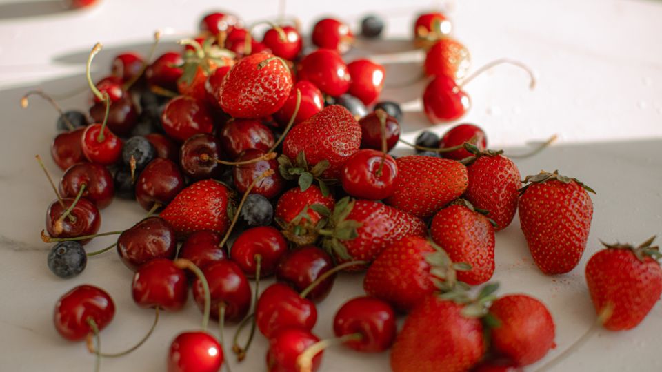Friss, piros eprek, cseresznyék és áfonyák egy fehér felületen, tökéletes tavaszi gyümölcsök.