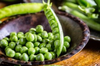 Friss, zöld borsók egy tálban, körülöttük borsós Hüvelyek.