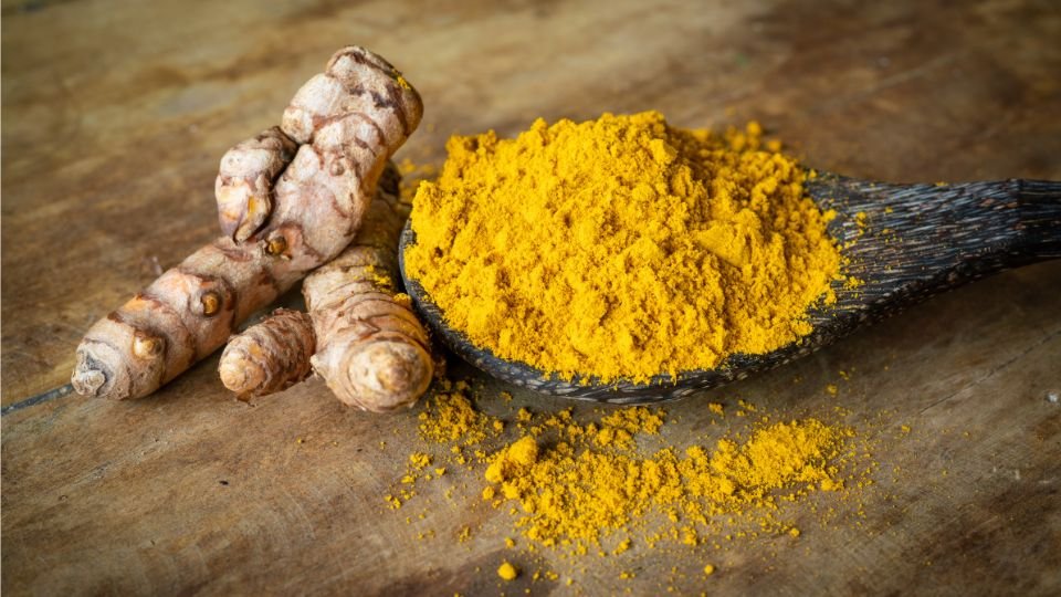 Friss gyömbérgyökér és porított kurkuma egy fakanálon, természetes környezetben.