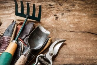 Kerti szerszámok, beleértve a kesztyűt, ásót és metszőollót, fa asztalon.