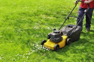 Tavaszi fűnyírás közben egy férfi dolgozik a zöld pázsiton, virágok között.