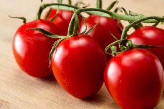 Friss, érett eper paradicsomok csoportja, zöld szárral, fából készült felületen.