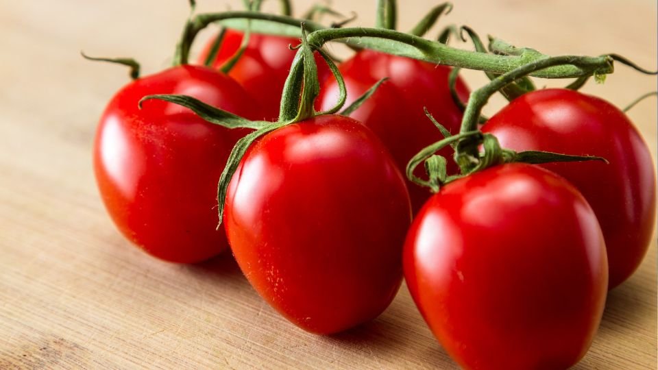 Friss, érett eper paradicsomok csoportja, zöld szárral, fából készült felületen.