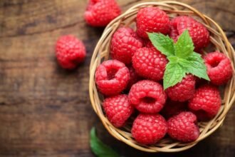 Friss, piros málna egy kosárban, zöld mentalevéllel díszítve.