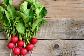 Friss retek zöld levelekkel, natúr fafelületen elhelyezve.