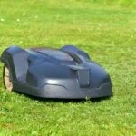 Egy robotfűnyíró zöld pázsiton, napfényben dolgozik.