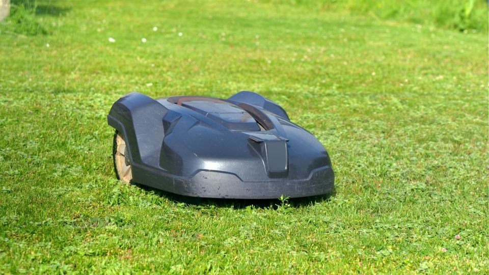 Egy robotfűnyíró zöld pázsiton, napfényben dolgozik.