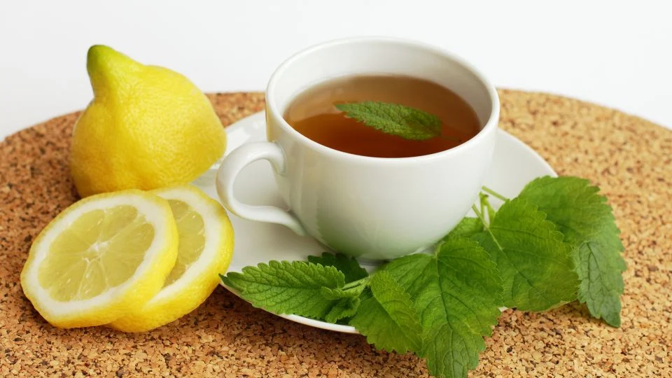 Frissítő citromfű tea és citrom Egy csésze citromfű tea, friss citromszeletek és citrom gyümölcs mellett, barátságos hangulatban.