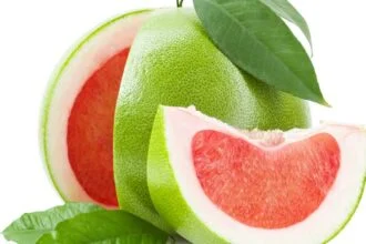 Friss pomelo gyümölcs, zöld héjjal, belsejében rózsaszín hús található, zöld levelekkel díszítve.