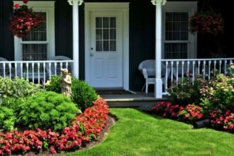 Egy szép előkert virágokkal és zöld növényekkel, kellemes hangulatú bejárati ajtó előtt.