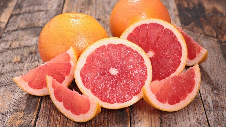 Friss grapefruitok és szeleteik egy rusztikus faasztalon, színes és ízletes látvány.