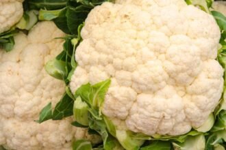 Friss karfiolok zöld levelekkel, gazdag színű és textúrájú.