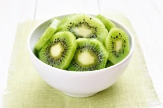 Friss, szeletelt kiwi egy fehér tálban, zöld alátéten.