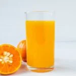 Friss narancslé egy pohárban, mellette félbevágott narancs és narancsok.