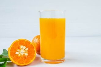 Friss narancslé egy pohárban, mellette félbevágott narancs és narancsok.