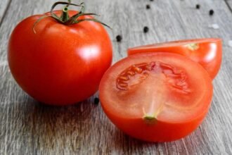 Friss, piros paradicsom, egy egész és egy fél paradicsom, fás háttér előtt.
