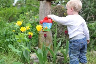 Egy kisgyermek locsolja a színes virágokat a kertben, miközben a természet szépségeit élvezi.