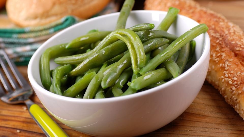 Friss, zöld zöldbab egy fehér tálban, friss kenyér mellett.