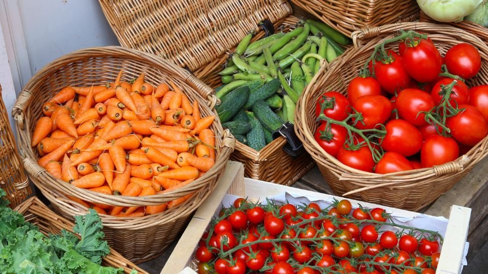 Friss zöldségek, mint sárgarépa, paradicsom és uborka, fonott kosarakban, zöldséges standon.