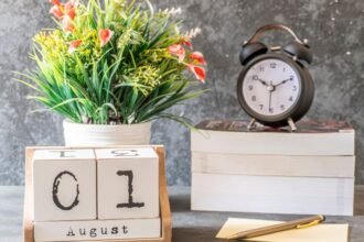Augusztusi naptár, virágcserép és óra egy íróasztalon.