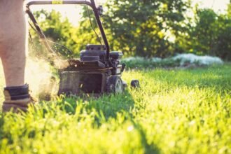 Egy ember fűnyíróval dolgozik a zöld kertben, napsütésben.