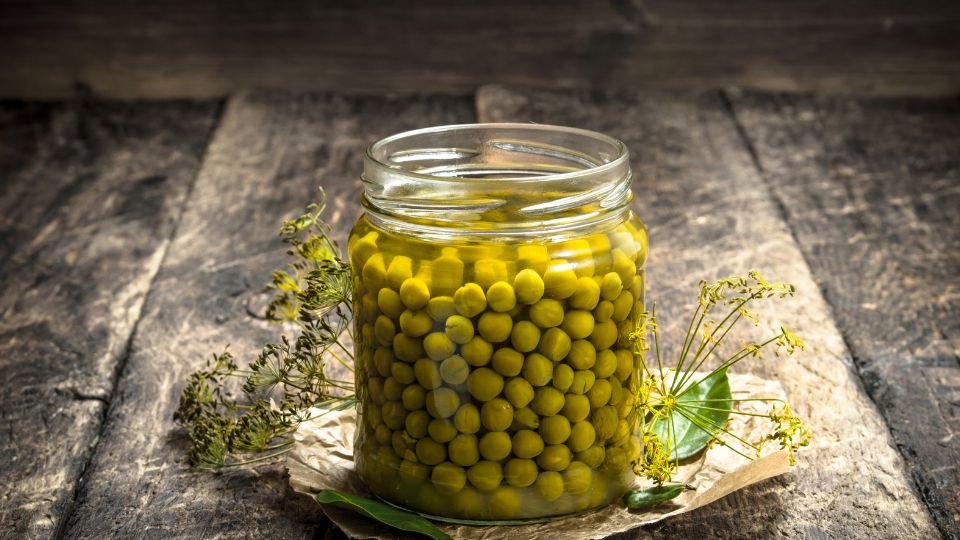 Egy üveg zöldborsó, friss fűszernövényekkel díszítve, fa háttér előtt.