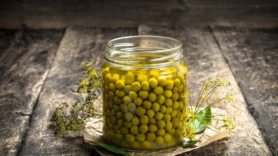 Egy üveg zöldborsó, friss fűszernövényekkel díszítve, fa háttér előtt.