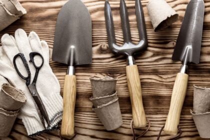 Kerti szerszámok, mint lapát, gereblye és metszőolló, egy faasztalon.