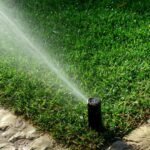 Öntözőrendszer működés közben, zöld fűvel és kövezett sétánnyal.