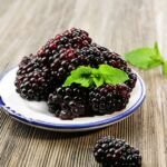 Friss szederbogyók egy tányéron, zöld mentalevéllel díszítve.