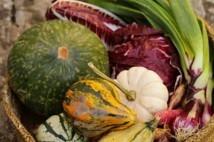 Különböző őszi zöldségek és fűszernövények egy kosárban, köztük tökök, póréhagyma és saláták.