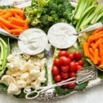 Friss zöldségek, mint répa, brokkoli, zeller és karfiol, egy tálon, joghurtos öntettel tálalva.