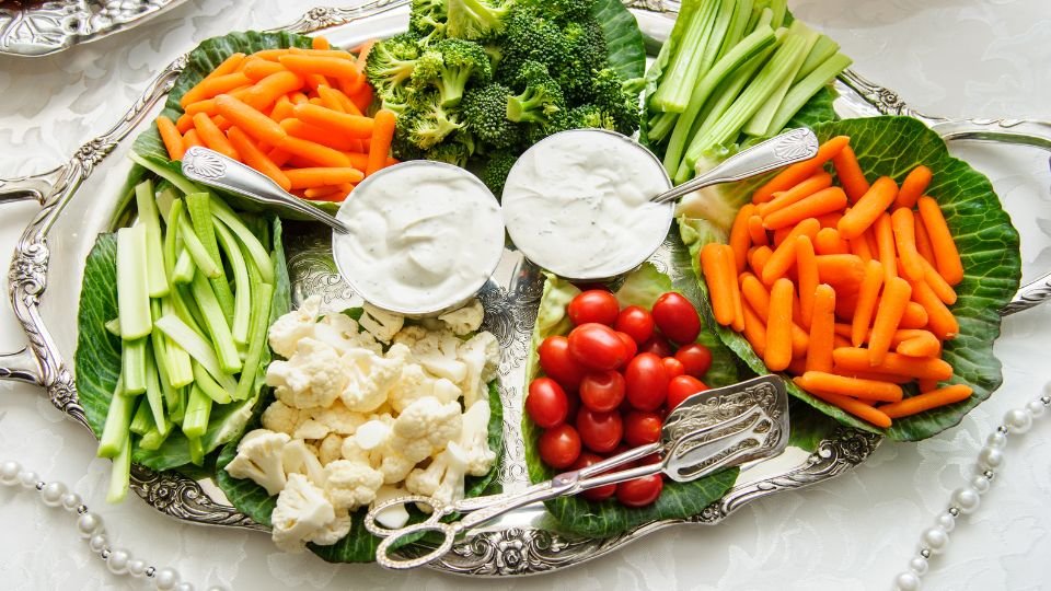 Friss zöldségek, mint répa, brokkoli, zeller és karfiol, egy tálon, joghurtos öntettel tálalva.