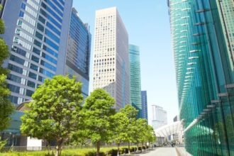 Zöld fák és modern felhőkarcolók egy városi környezetben, napfényben.