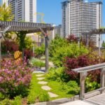 Egy városi tetőkert, tele virágokkal és zöld növényekkel, háttérben modern épületekkel.