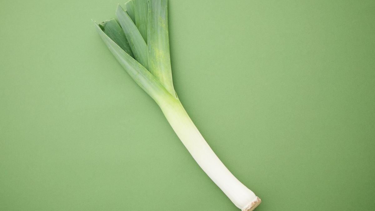 Friss póréhagyma, zöld levelekkel és fehér szárral, zöld háttéren.