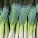 Friss, zöld póréhagymák sorakoznak egy piaci standon, készen a felhasználásra.