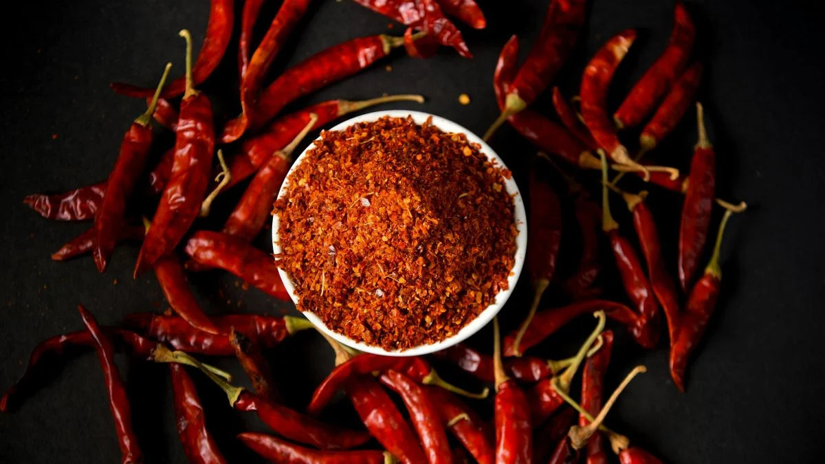 Friss, piros chilik és chili por egy fehér tálban, amely a kerti betakarítás gazdag termését szimbolizálja.